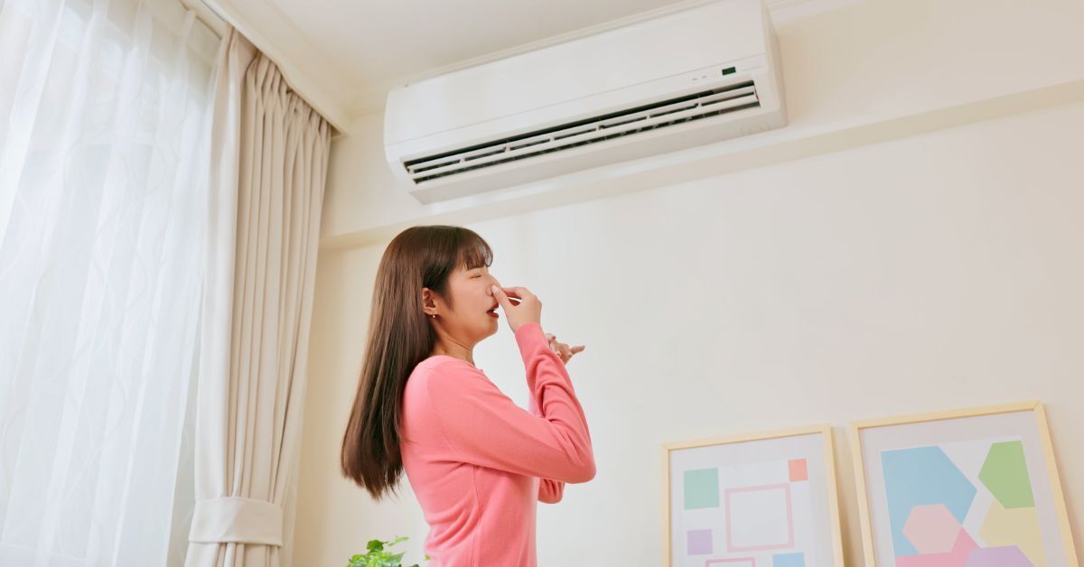 Woman holding her nose at a musty smell from a wall-mounted AC unit